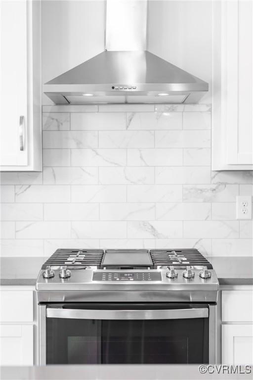 kitchen featuring tasteful backsplash, wall chimney range hood, white cabinets, and gas stove