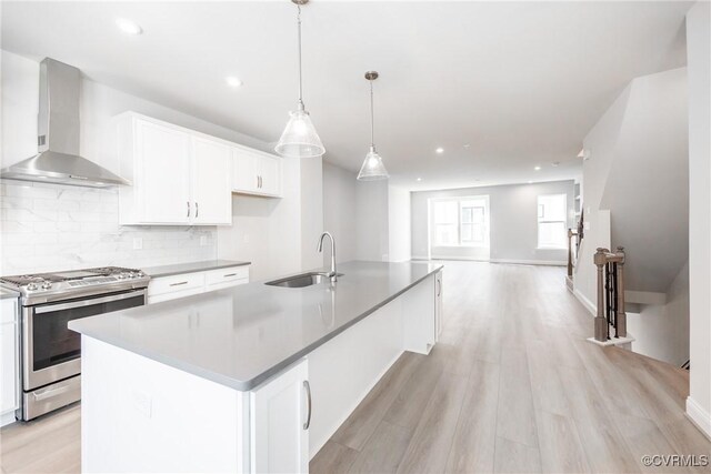 kitchen featuring white cabinets, wall chimney exhaust hood, a sink, stainless steel gas range oven, and decorative backsplash