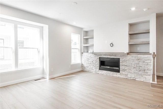 unfurnished living room with a fireplace, baseboards, wood finished floors, and built in shelves