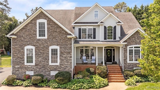 view of front of house featuring a porch, a standing seam roof, a shingled roof, metal roof, and stone siding
