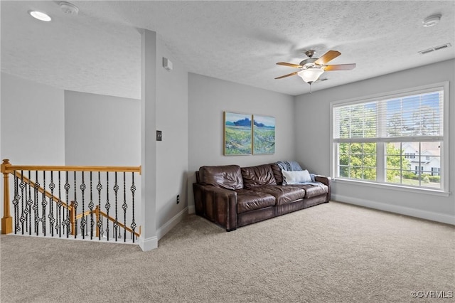 living area featuring a textured ceiling, visible vents, baseboards, carpet floors, and a ceiling fan