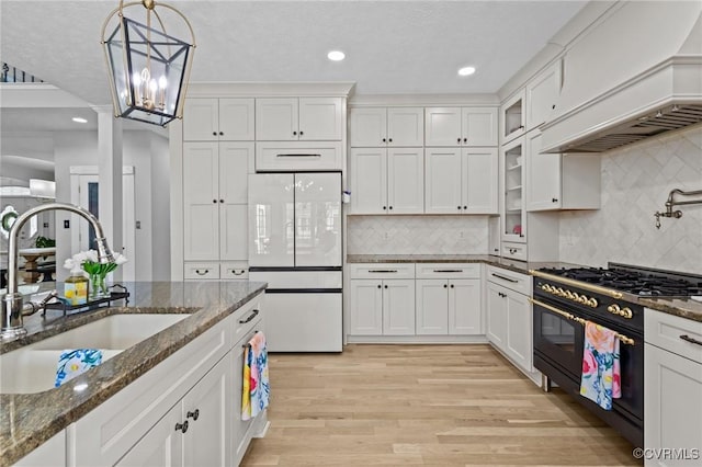 kitchen with double oven range, white cabinetry, custom range hood, a sink, and freestanding refrigerator
