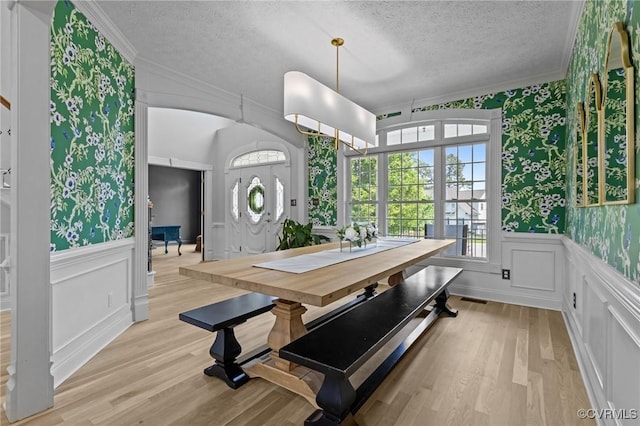 dining area featuring wallpapered walls, light wood-style flooring, a textured ceiling, and crown molding