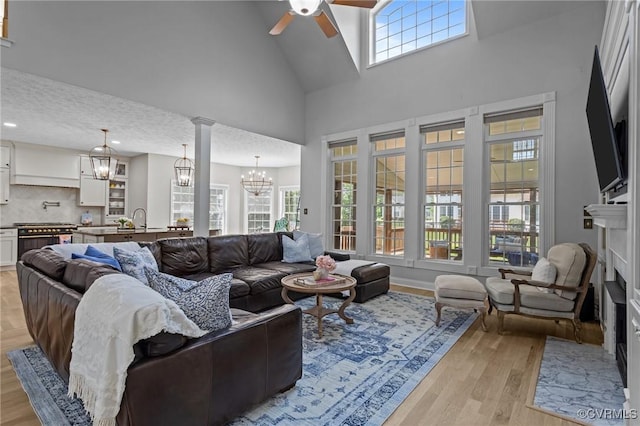 living area with a fireplace with flush hearth, light wood-style flooring, high vaulted ceiling, and ceiling fan with notable chandelier