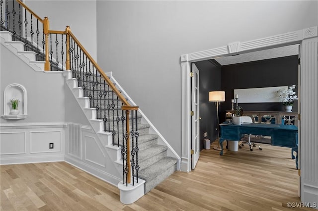 stairs with visible vents, wood finished floors, a high ceiling, and a decorative wall