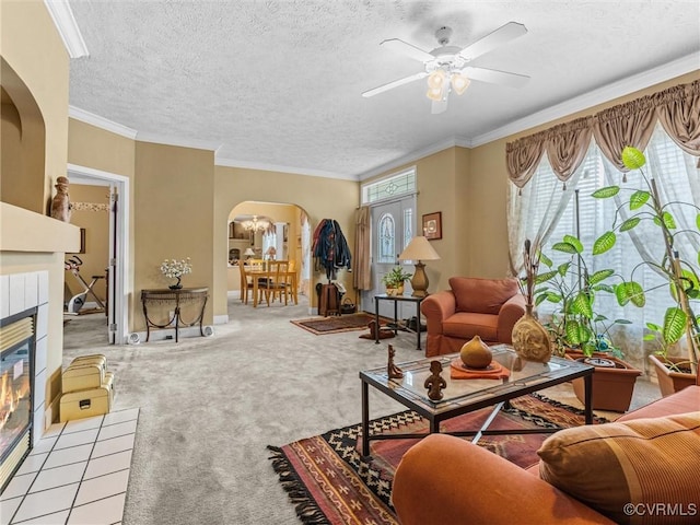 living room featuring carpet floors, a ceiling fan, a fireplace, arched walkways, and ornamental molding