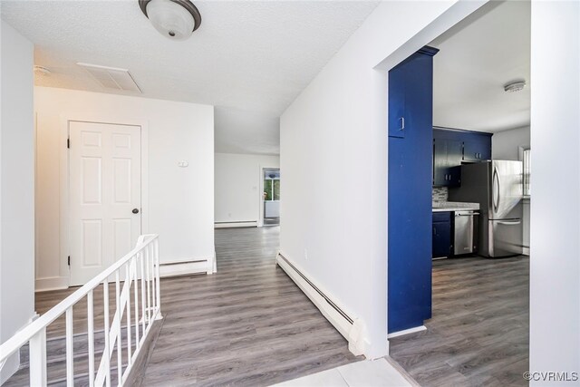 hall with a baseboard heating unit, dark wood finished floors, and visible vents