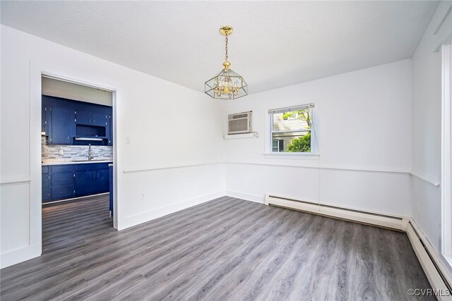 empty room featuring an inviting chandelier, wood finished floors, a baseboard heating unit, a wall unit AC, and a sink