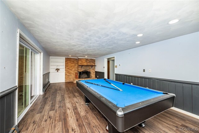 rec room featuring recessed lighting, dark wood-style flooring, a brick fireplace, and a wainscoted wall