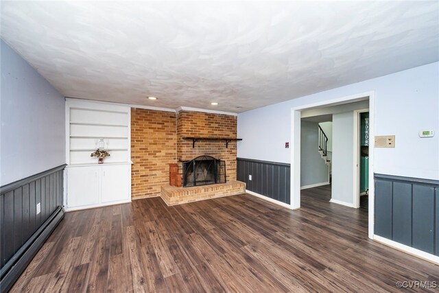 unfurnished living room with a wainscoted wall, baseboard heating, stairs, and built in shelves