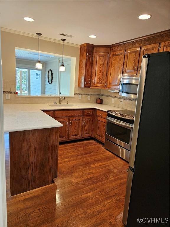 kitchen featuring a sink, appliances with stainless steel finishes, dark wood finished floors, brown cabinets, and decorative light fixtures