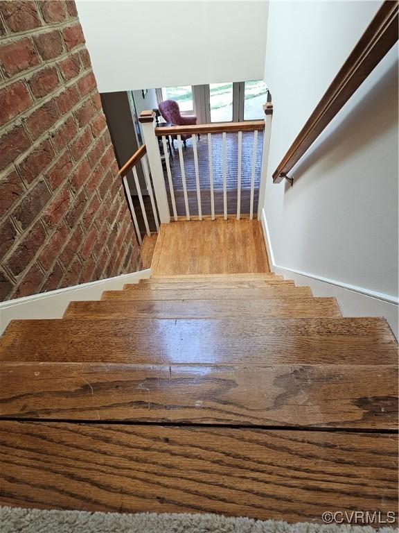 stairway with wood finished floors and brick wall