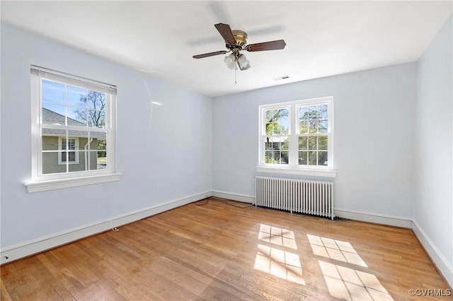 empty room featuring radiator heating unit, a wealth of natural light, baseboards, and wood finished floors