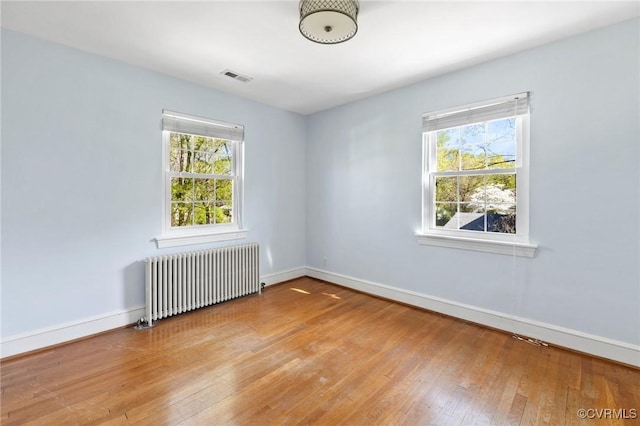 empty room featuring hardwood / wood-style floors, radiator heating unit, baseboards, and visible vents