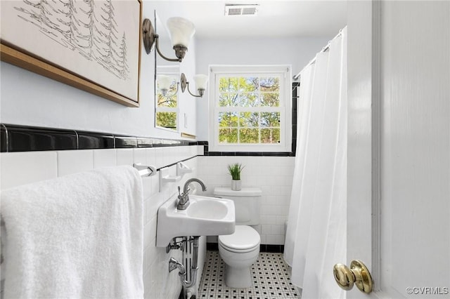 bathroom featuring curtained shower, toilet, visible vents, wainscoting, and tile walls