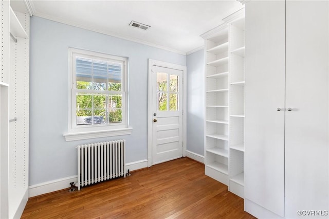 doorway featuring radiator heating unit, visible vents, ornamental molding, and wood finished floors
