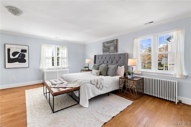 bedroom with visible vents, baseboards, radiator, and wood finished floors