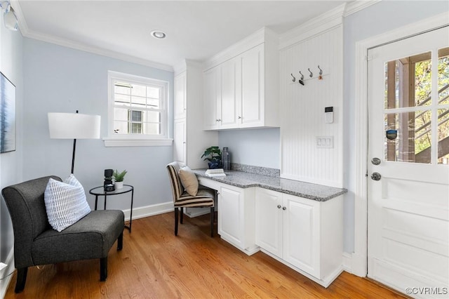 office area with light wood-style flooring, built in study area, crown molding, and baseboards