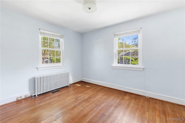 spare room with visible vents, radiator heating unit, hardwood / wood-style flooring, and baseboards