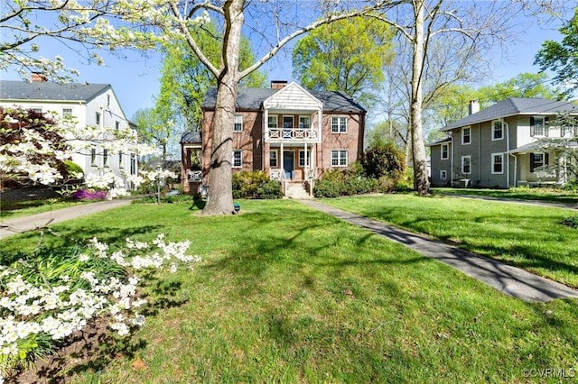 view of front facade featuring a front yard, a chimney, and a balcony