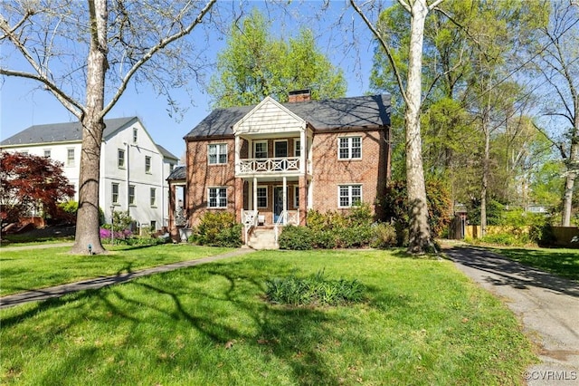 view of front of property featuring a front yard, a chimney, brick siding, and a balcony