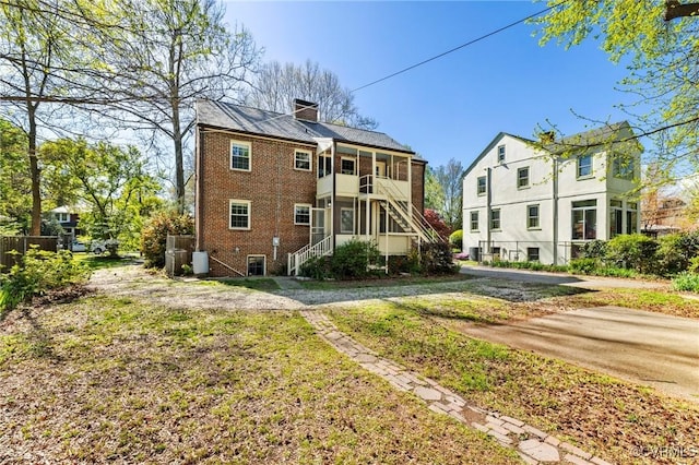 back of house featuring a sunroom, a lawn, brick siding, a chimney, and stairs