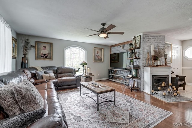 living room with wood finished floors, a textured ceiling, ceiling fan, a fireplace, and baseboards