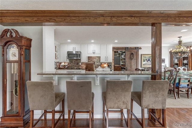 kitchen with stainless steel microwave, dark stone counters, backsplash, white cabinetry, and a kitchen bar