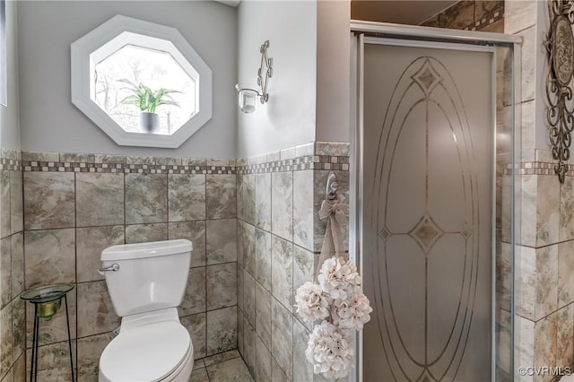 bathroom with tile walls, a wainscoted wall, a stall shower, and toilet