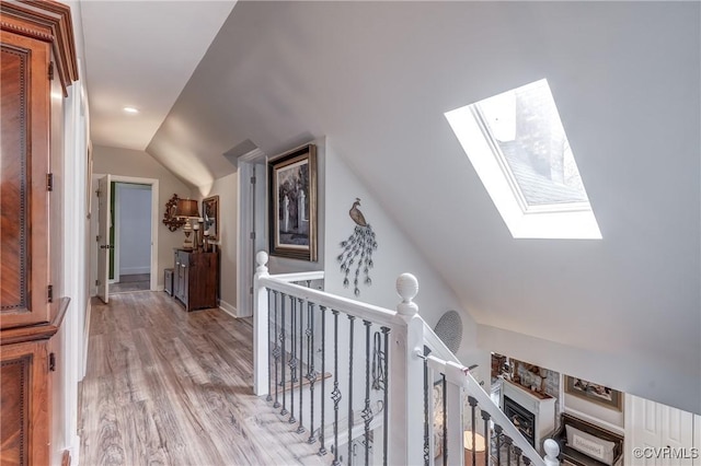 corridor featuring vaulted ceiling with skylight, an upstairs landing, and light wood-style floors