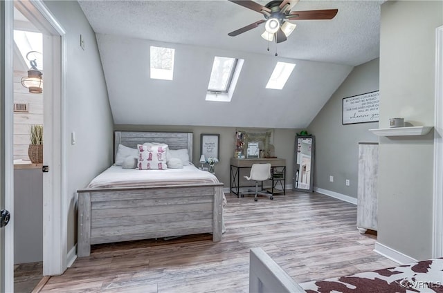 bedroom featuring wood finished floors, a ceiling fan, baseboards, vaulted ceiling with skylight, and a textured ceiling