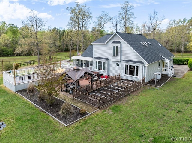 back of house with roof with shingles, a lawn, fence, and a deck