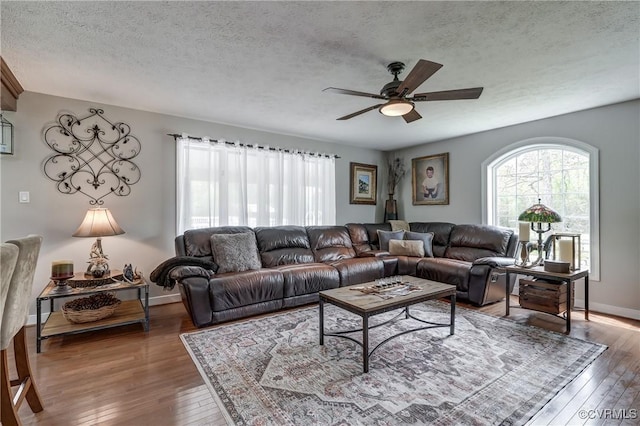 living area featuring wood-type flooring, a textured ceiling, a ceiling fan, and baseboards