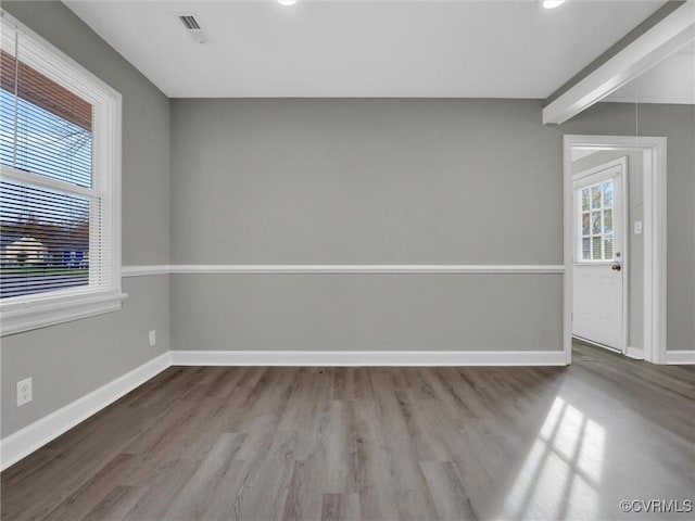 empty room featuring baseboards, visible vents, wood finished floors, and beam ceiling