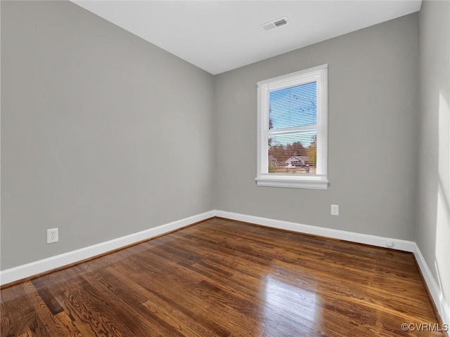 empty room featuring baseboards, visible vents, and wood finished floors