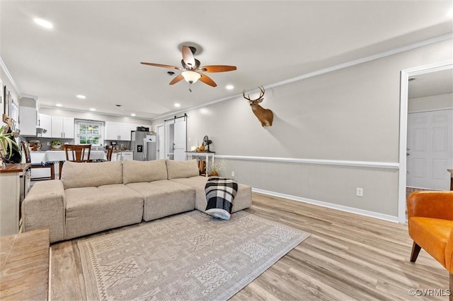 living area featuring a ceiling fan, light wood-type flooring, a barn door, ornamental molding, and recessed lighting