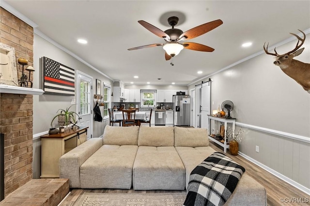 living area featuring crown molding, a barn door, light wood-style flooring, and ceiling fan