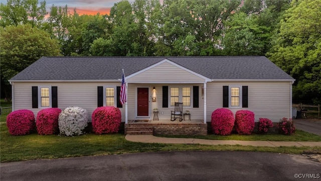 ranch-style house featuring covered porch, a shingled roof, and a front lawn