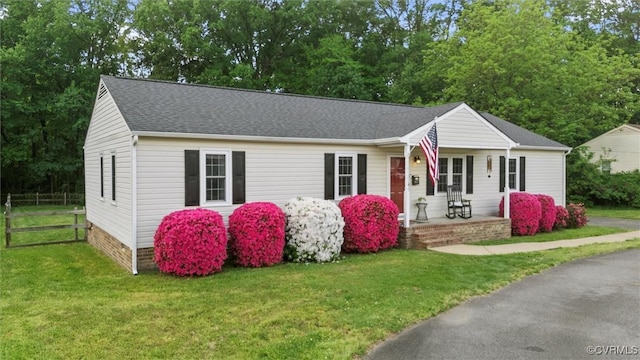 ranch-style home featuring fence, covered porch, a shingled roof, and a front yard