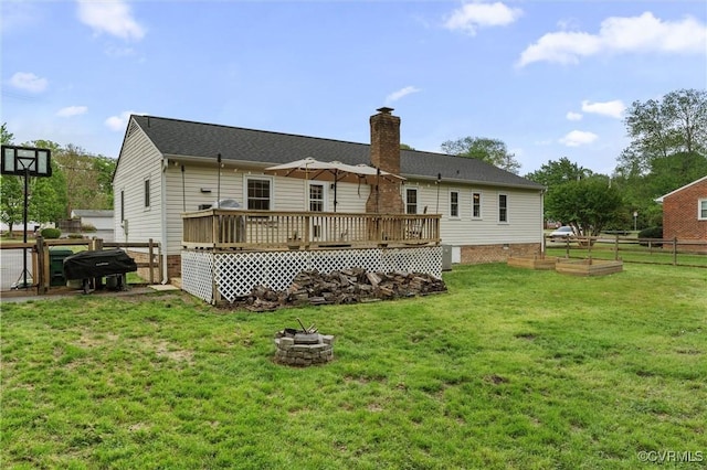 rear view of property featuring fence, an outdoor fire pit, a wooden deck, a chimney, and a lawn