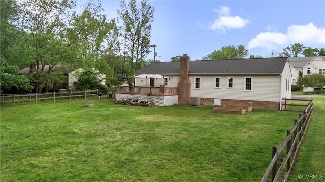 rear view of house with a chimney, a lawn, a deck, cooling unit, and a fenced backyard