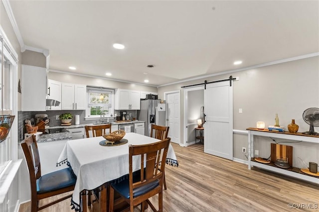 dining space with crown molding, a barn door, baseboards, recessed lighting, and light wood-style flooring