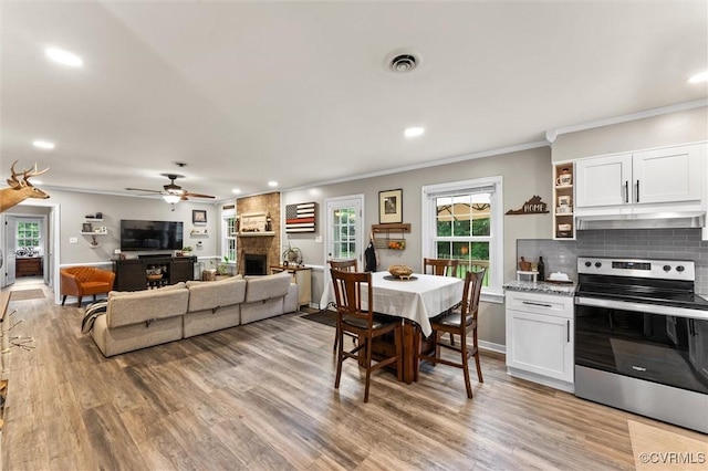 dining space featuring crown molding, a large fireplace, a ceiling fan, recessed lighting, and light wood-type flooring