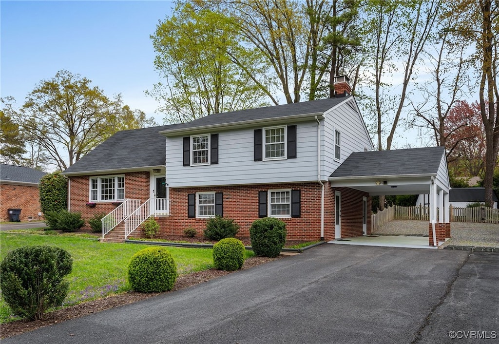 tri-level home with a chimney, aphalt driveway, brick siding, a front yard, and fence