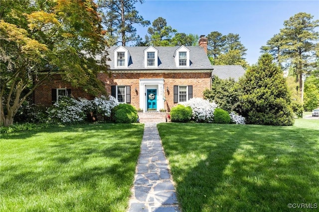 cape cod-style house with a chimney, brick siding, and a front yard