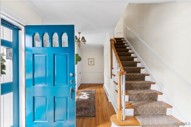 entryway featuring a baseboard heating unit, ornamental molding, wood finished floors, and stairs
