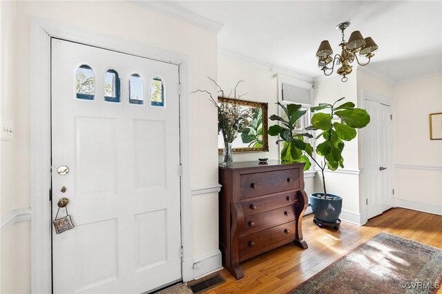 foyer entrance featuring visible vents, baseboards, an inviting chandelier, wood finished floors, and ornamental molding