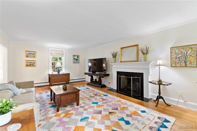 living area with baseboard heating, crown molding, wood finished floors, a baseboard heating unit, and a fireplace with flush hearth