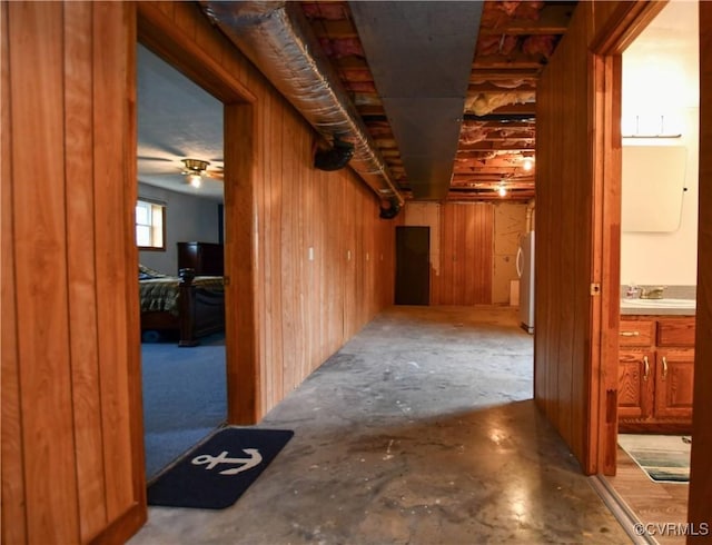 hallway with unfinished concrete floors, a sink, and wooden walls