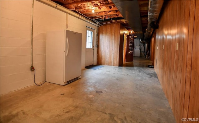 below grade area with freestanding refrigerator, concrete block wall, and wooden walls